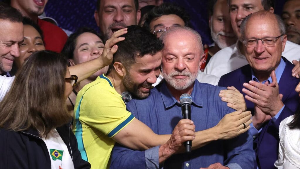Lula da Silva con un micrófono, acompañado por aliados y simpatizantes que celebran su triunfo electoral en Brasil.
