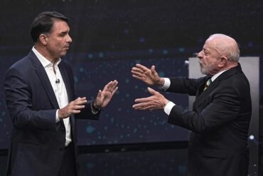 Lula da Silva y Flávio Bolsonaro frente a frente durante un debate presidencial en Brasil, con gestos de confrontación.
