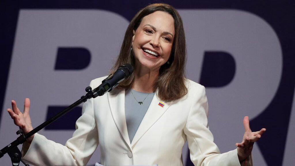 María Corina Machado, líder opositora venezolana, sonríe con los brazos abiertos frente a un micrófono