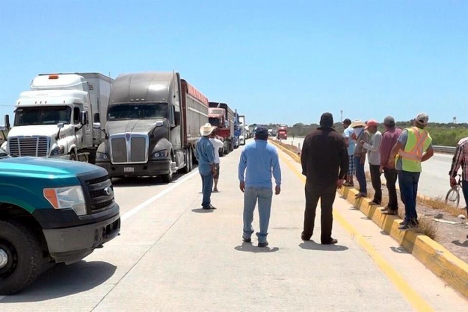 Operadores del autotransporte de carga de pie sobre una carretera junto a tráileres detenidos durante una protesta del gremio
