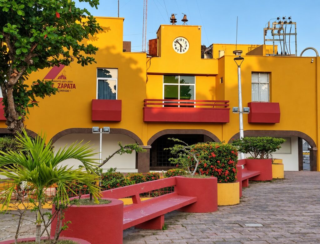 Fachada amarilla del Palacio Municipal de Emiliano Zapata, Tabasco, con reloj central, arcos de acceso y jardineras.