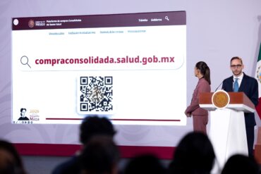 Pantalla de la mañanera con la Plataforma de compras consolidadas del sector Salud, su dirección web compraconsolidada.salud.gob.mx y un código QR, junto a dos funcionarios.