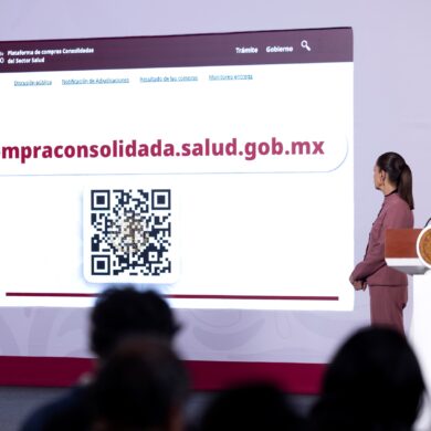 Pantalla de la mañanera con la Plataforma de compras consolidadas del sector Salud, su dirección web compraconsolidada.salud.gob.mx y un código QR, junto a dos funcionarios.