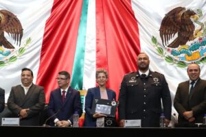 Representante de la embajada de Israel sostiene un reconocimiento de Policías Celestiales durante una ceremonia en la Cámara de Diputados, ante la bandera de México.