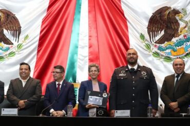 Representante de la embajada de Israel sostiene un reconocimiento de Policías Celestiales durante una ceremonia en la Cámara de Diputados, ante la bandera de México.
