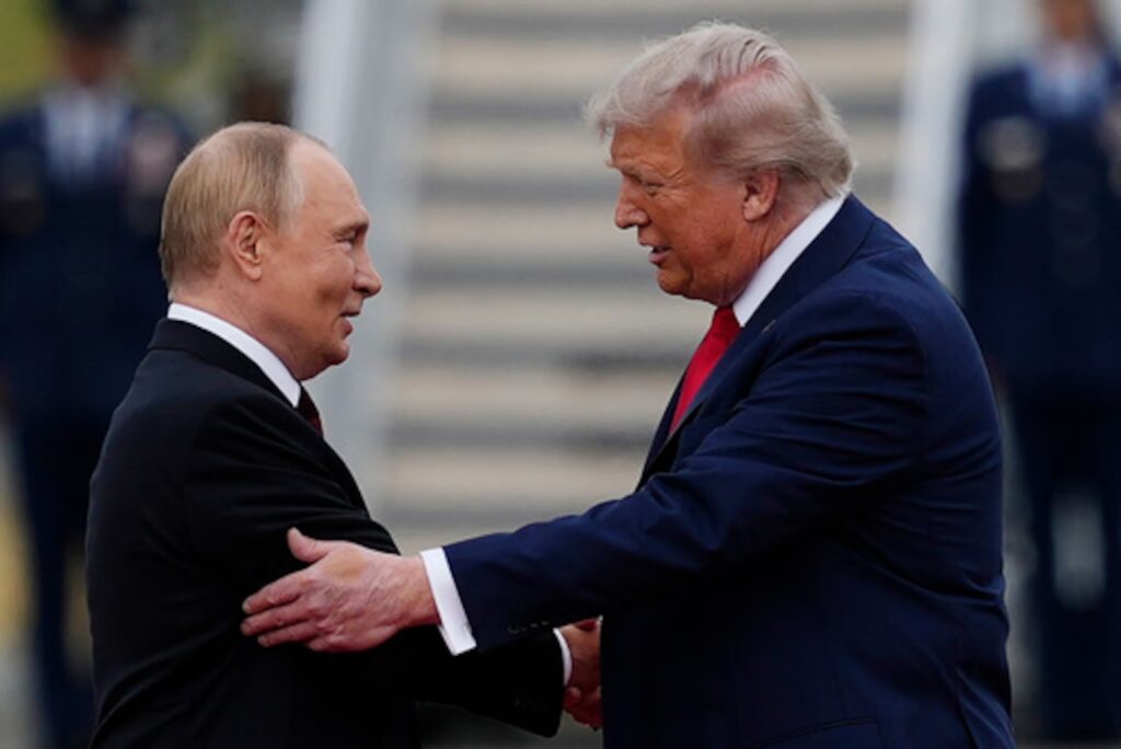 Vladímir Putin y Donald Trump se saludan con un apretón de manos frente a una escalinata, con un guardia de honor desenfocado al fondo