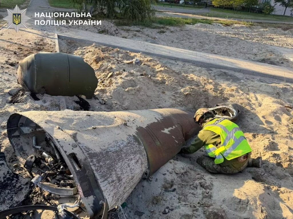 Agente uniformado inspecciona grandes fragmentos de un proyectil sobre terreno arenoso, en una imagen difundida por la Policía Nacional de Ucrania.