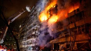 Edificio envuelto en llamas durante un incendio de gran magnitud, mientras bomberos utilizan una plataforma elevada para combatir el fuego.