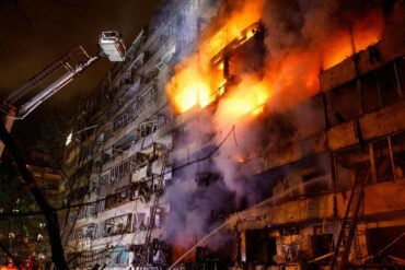 Edificio envuelto en llamas durante un incendio de gran magnitud, mientras bomberos utilizan una plataforma elevada para combatir el fuego.