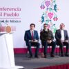 La presidenta Claudia Sheinbaum habla desde el podio durante la conferencia matutina, con cuatro asistentes sentados detrás
