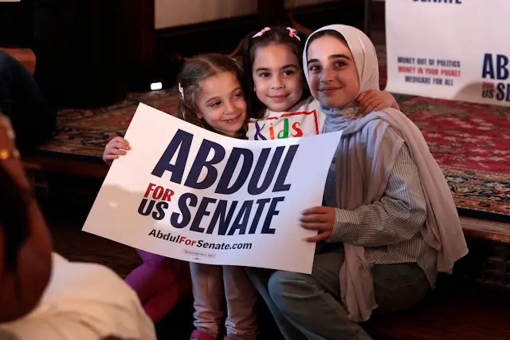 Tres jóvenes simpatizantes posan con un cartel electoral de Abdul El-Sayed al Senado de Estados Unidos; una de ellas lleva hiyab.