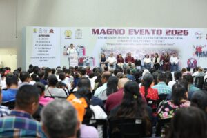 Orador en el podio del Magno Evento 2026 del SUTSET; el cartel del escenario enlista laptops, prótesis, licencias, gastos de titulación y lentes