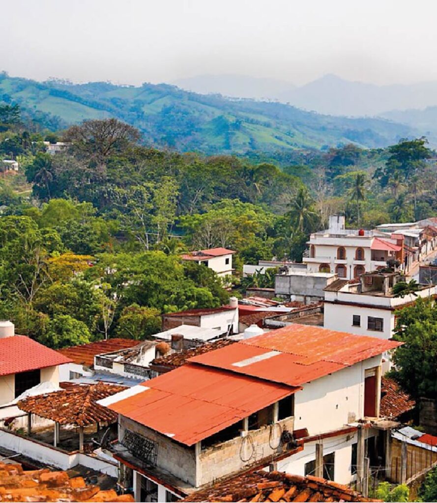 Vista elevada de Tacotalpa, Tabasco, con casas de techos rojos entre árboles y lomas verdes al fondo.
