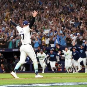 Un lanzador de los Rays de Tampa Bay levanta los brazos mientras sus compañeros salen corriendo del banquillo y la tribuna celebra el pase a la Serie Mundial