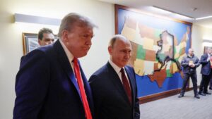 Donald Trump, serio, y Vladímir Putin, sonriente, caminan juntos por un pasillo frente a un mapa de madera de Estados Unidos