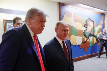 Donald Trump, serio, y Vladímir Putin, sonriente, caminan juntos por un pasillo frente a un mapa de madera de Estados Unidos