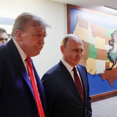 Donald Trump, serio, y Vladímir Putin, sonriente, caminan juntos por un pasillo frente a un mapa de madera de Estados Unidos