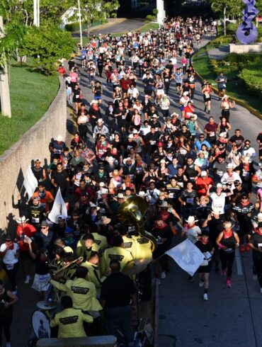 Multitud de corredores con sombreros y paliacates avanza junto a una banda con uniformes amarillos en la VaqueRun Tabasco 2026